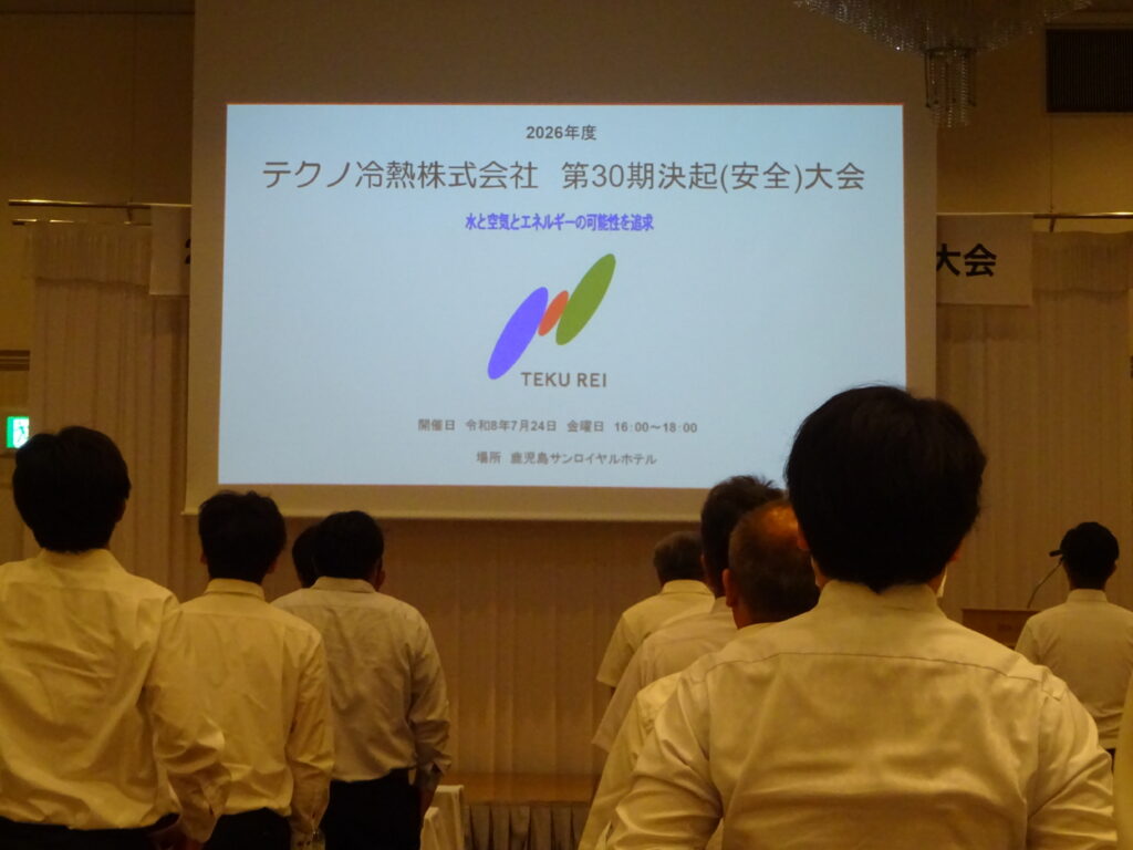 テクノ冷熱株式会社の第30期決起大会でスクリーンに映された次第を見つめる社員たち